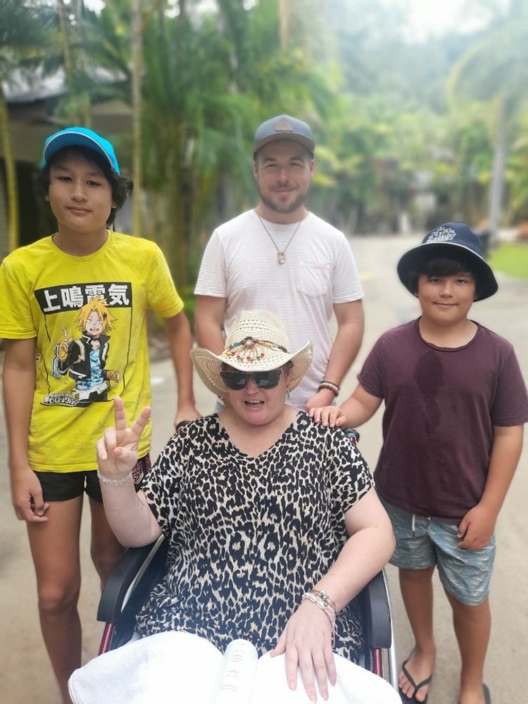 Lady with hat in a wheelchair with three teenage and young adult sons