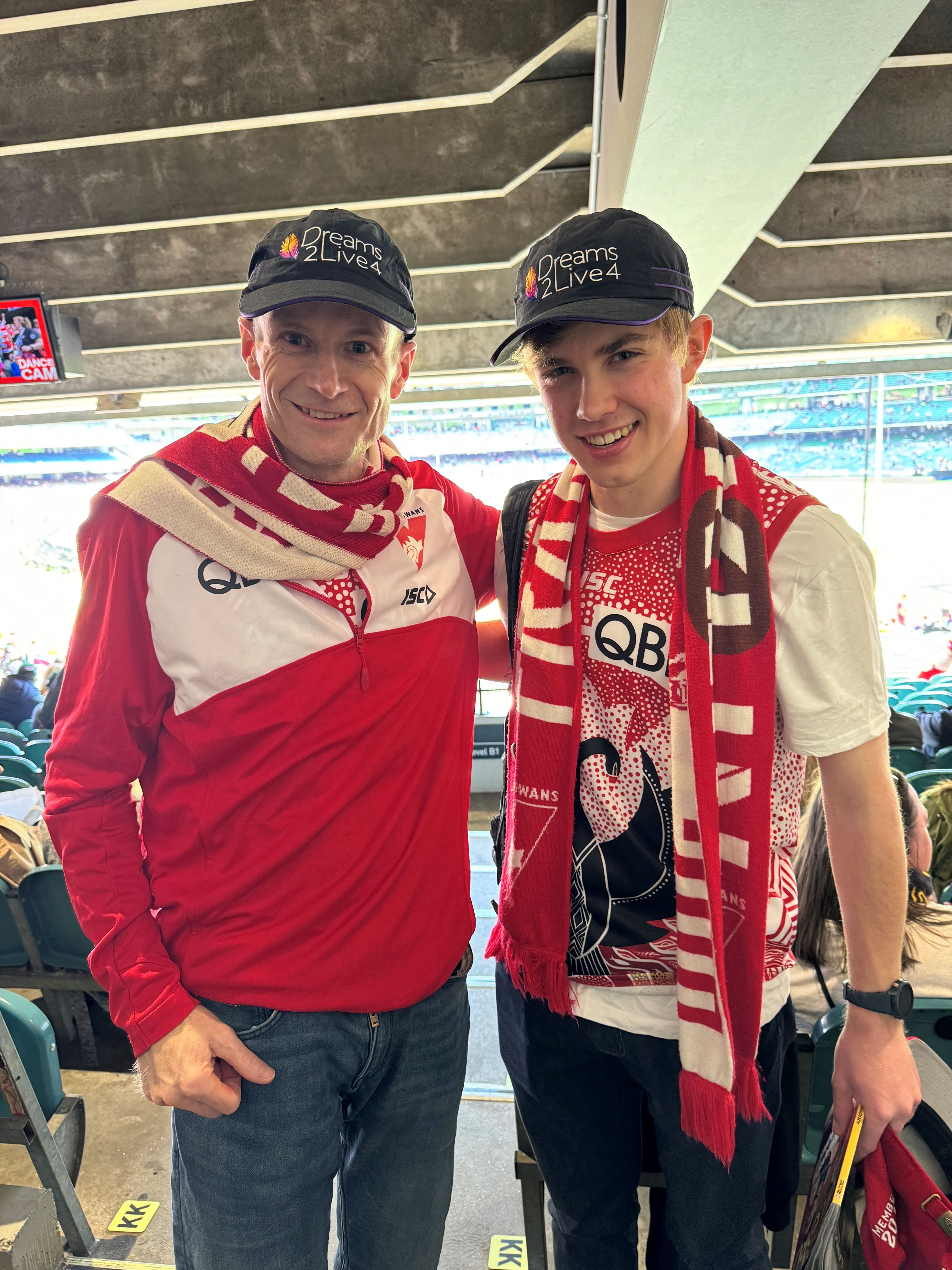 Man and young man in Dreams2Live4 cap and Sydney Swans jersey and scarf at the AFL grand final.